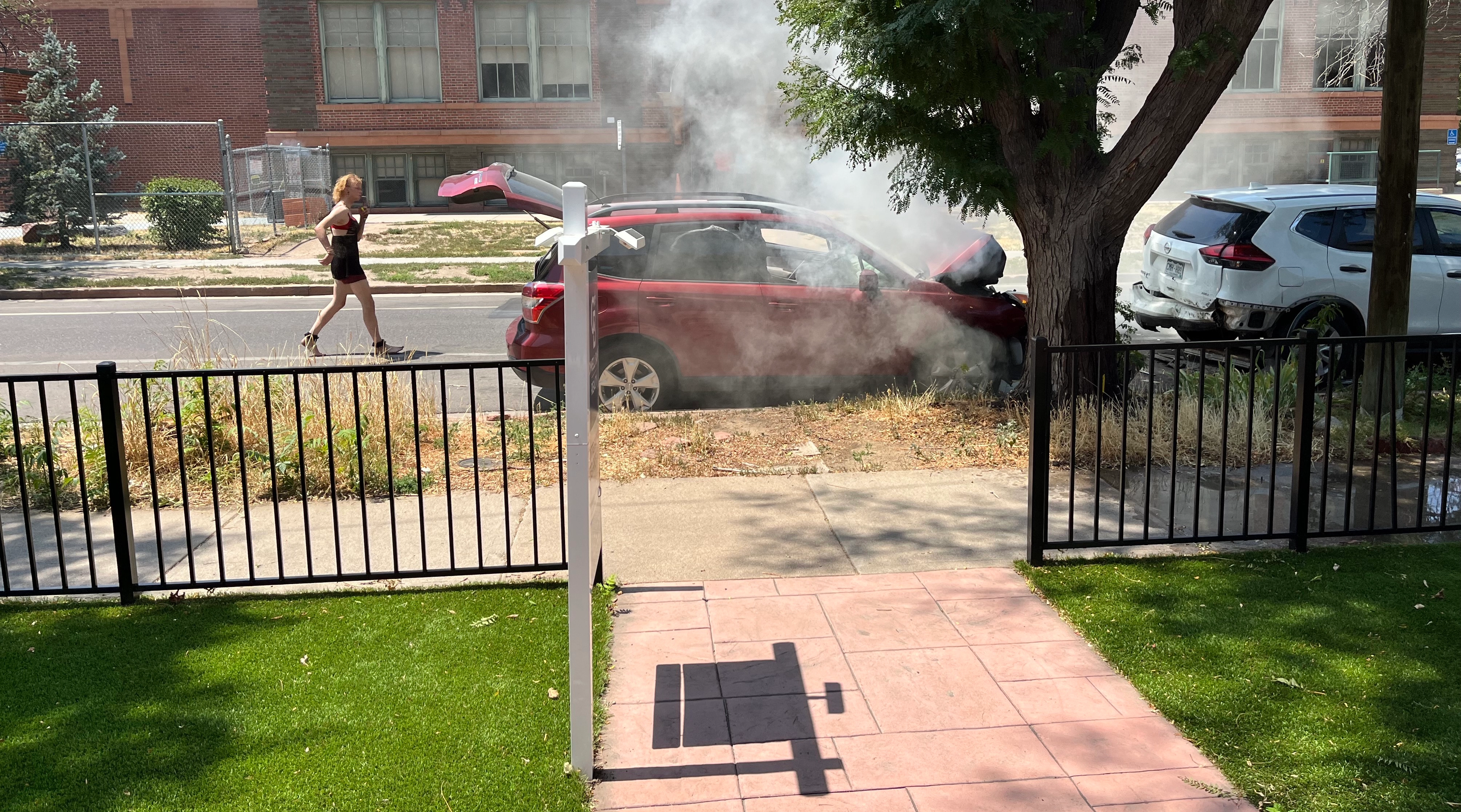 A car starting to catch fire in the street. The passenger smoking and pacing behind.